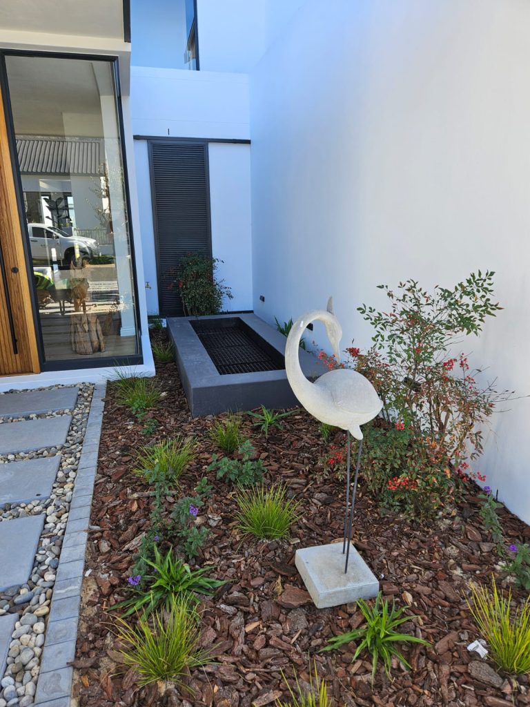 Flamingo statue surrounded by nandina (Nandina domestica) with red berries, ornamental grasses and low groundcovers by CSA Landscaping, leading precision landscapers in the Boland and Cape Winelands, at The Acres at Pearl Valley