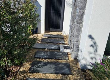 Stepping-stone pathway with gravel, olive shrub and ornamental grasses leading to a black gate by CSA Landscaping, the best in Boland and Cape Winelands landscaping, at The Acres at Pearl Valley, Paarl