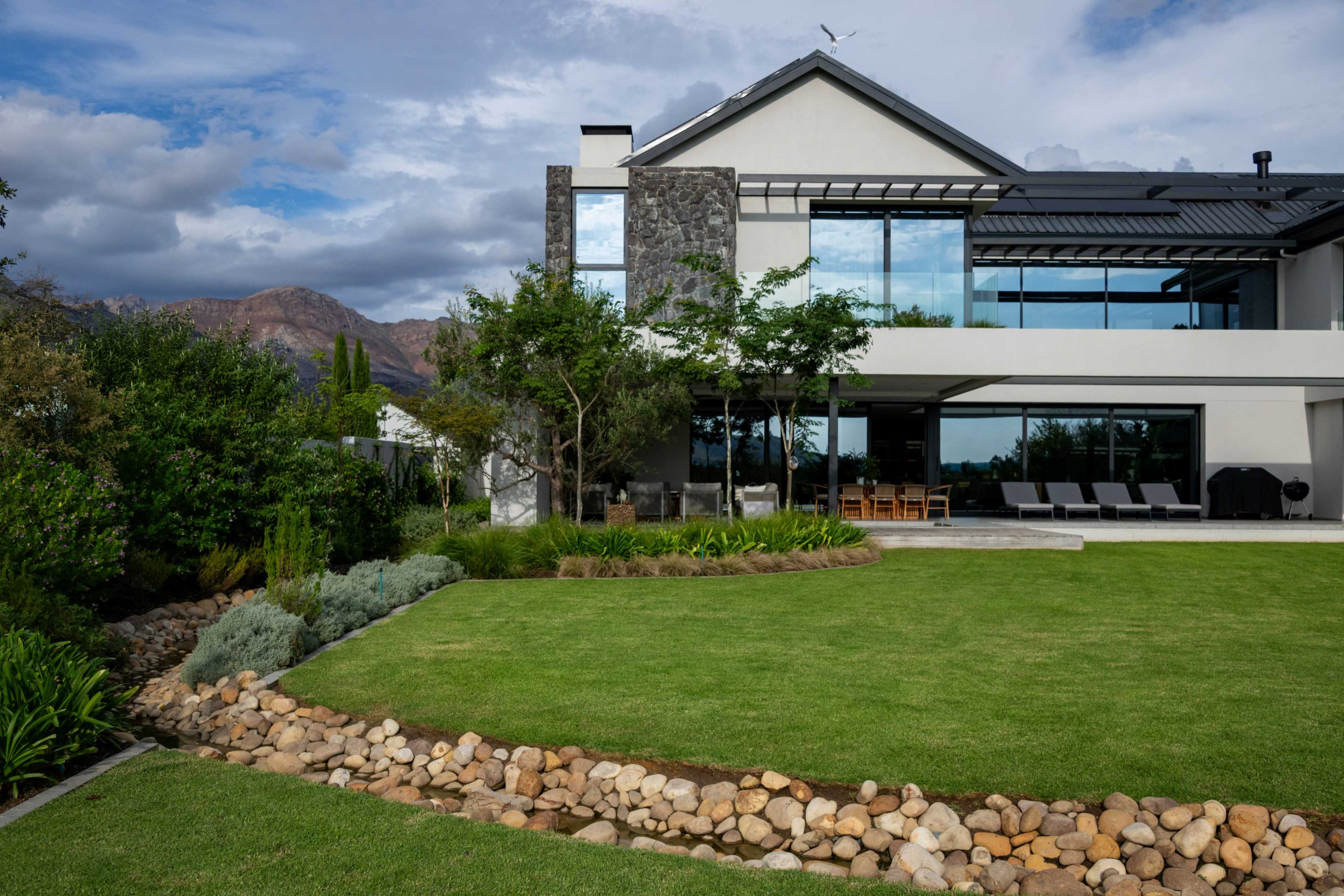 Timber boardwalk beside a feature tree planted in ornamental grasses and Dietes at the Van der Merwe garden, Val de Vie, Paarl, by CSA Landscaping, leading landscapers in the Boland and Cape Winelands