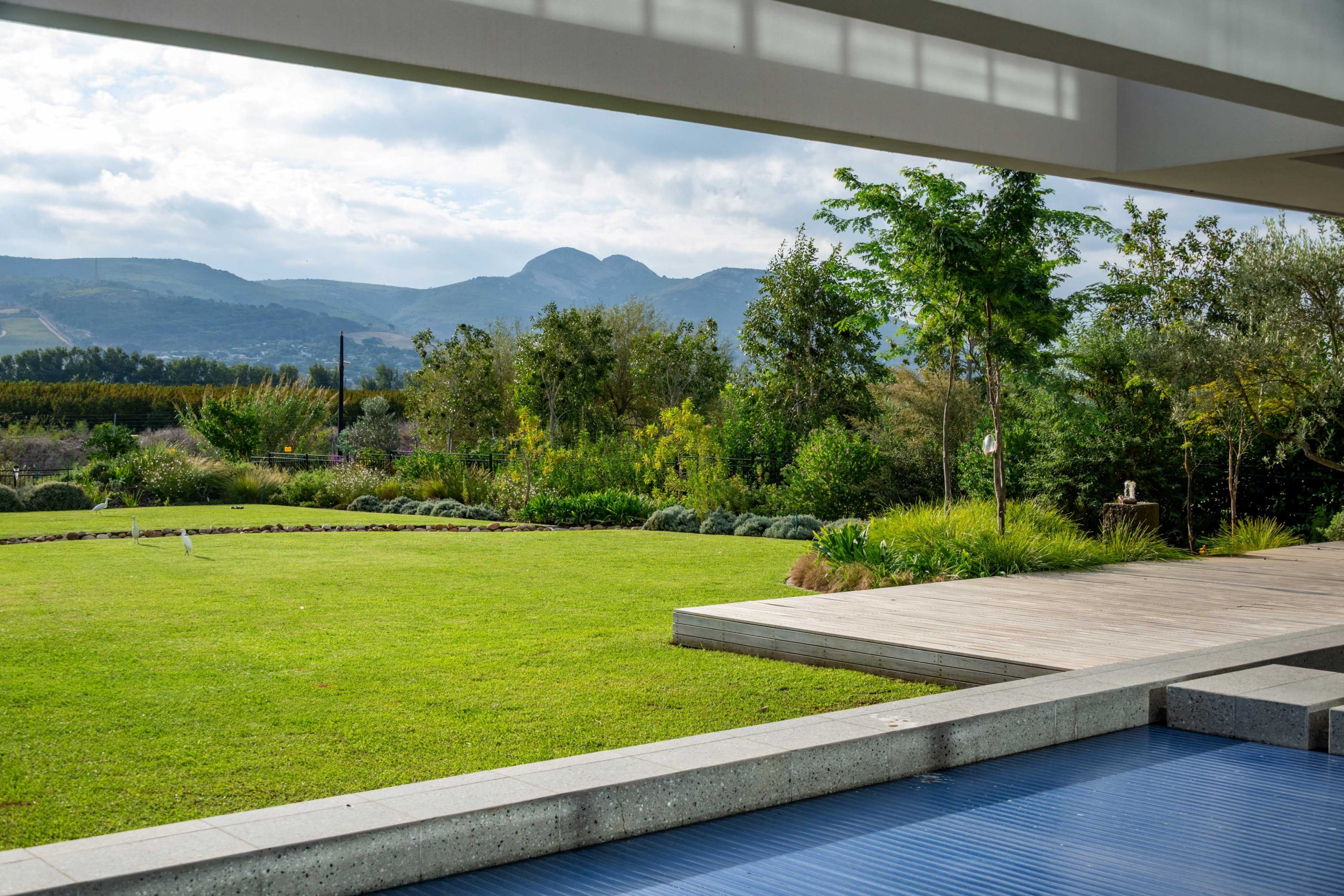 Timber deck and lawn garden with mountain views from the covered terrace at Val de Vie Estate, Paarl, by CSA Landscaping — leading landscapers in the Boland and Cape Winelands