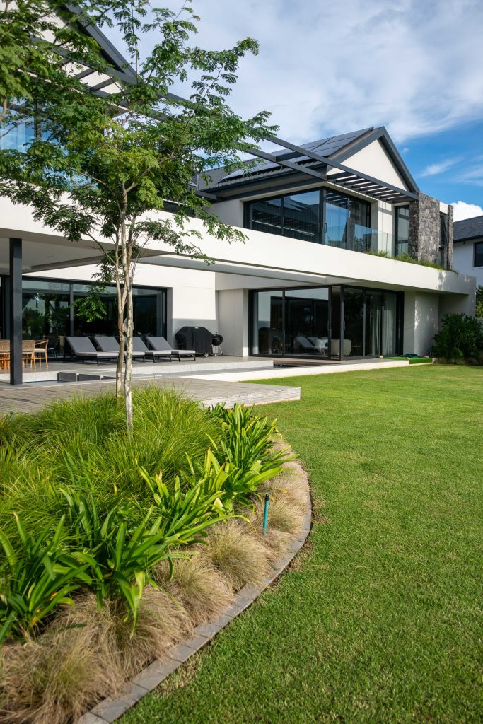 Curved lawn-edge bed of Dietes and ornamental grasses with a feature tree beside the outdoor terrace at Val de Vie Estate, Paarl, by CSA Landscaping — leading landscapers in the Boland and Cape Winelands