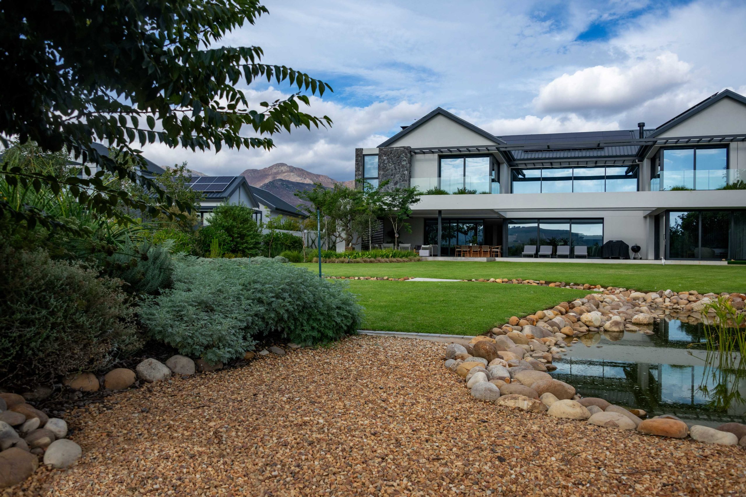 Gravel path beside silver Helichrysum planting and a river-stone edged circulating stream at a contemporary home in Val de Vie Estate, Paarl, by CSA Landscaping — leading landscapers in the Boland and Cape Winelands