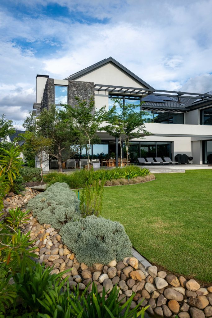 Silver Helichrysum and Dietes planted along the river-stone stream edge, with lawn and feature trees at a contemporary home in Val de Vie Estate, Paarl, by CSA Landscaping — leading landscapers in the Boland and Cape Winelands