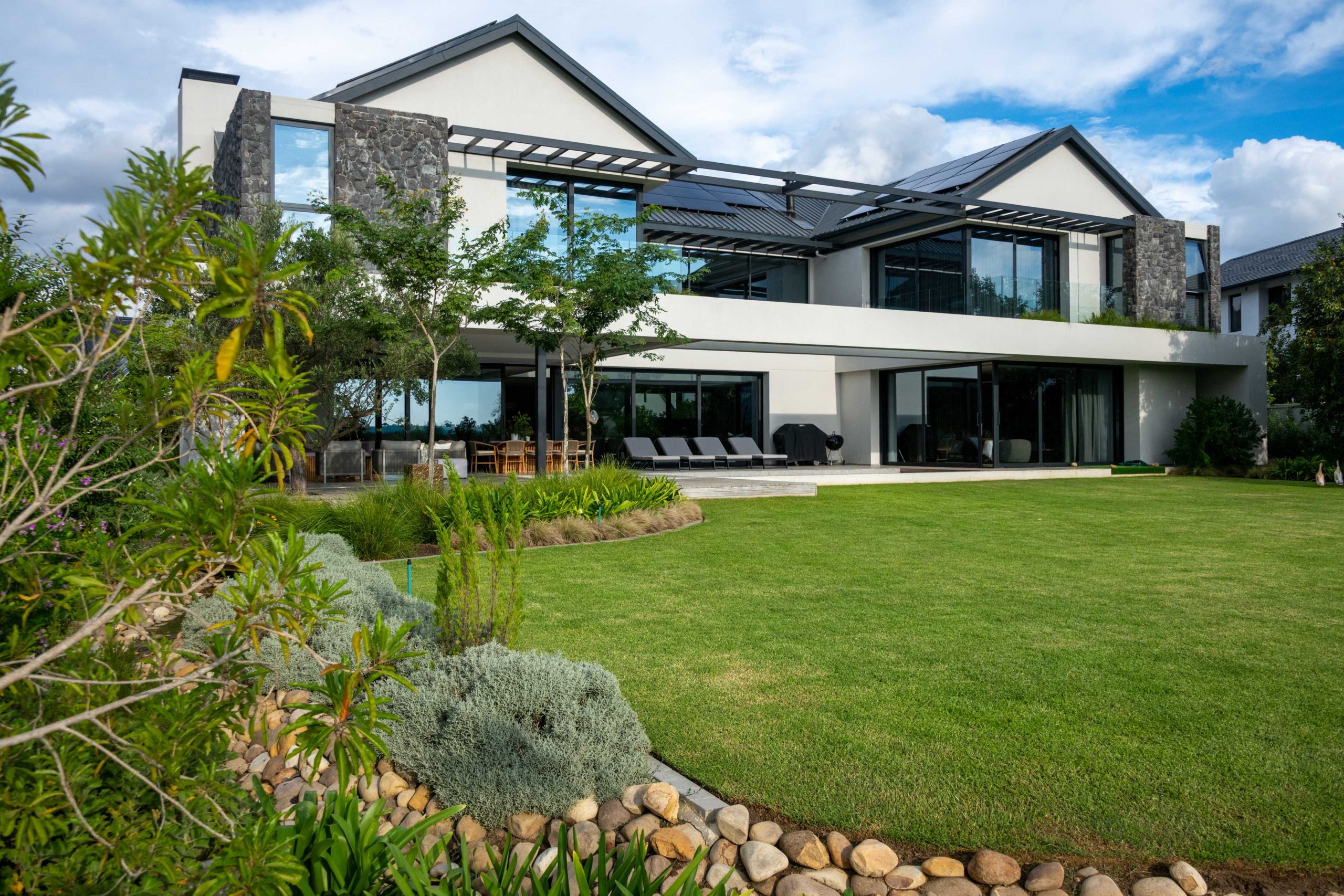 Layered Helichrysum, Dietes and river-stone stream edging the lawn in front of a contemporary home at Val de Vie Estate, Paarl, by CSA Landscaping — leading landscapers in the Boland and Cape Winelands