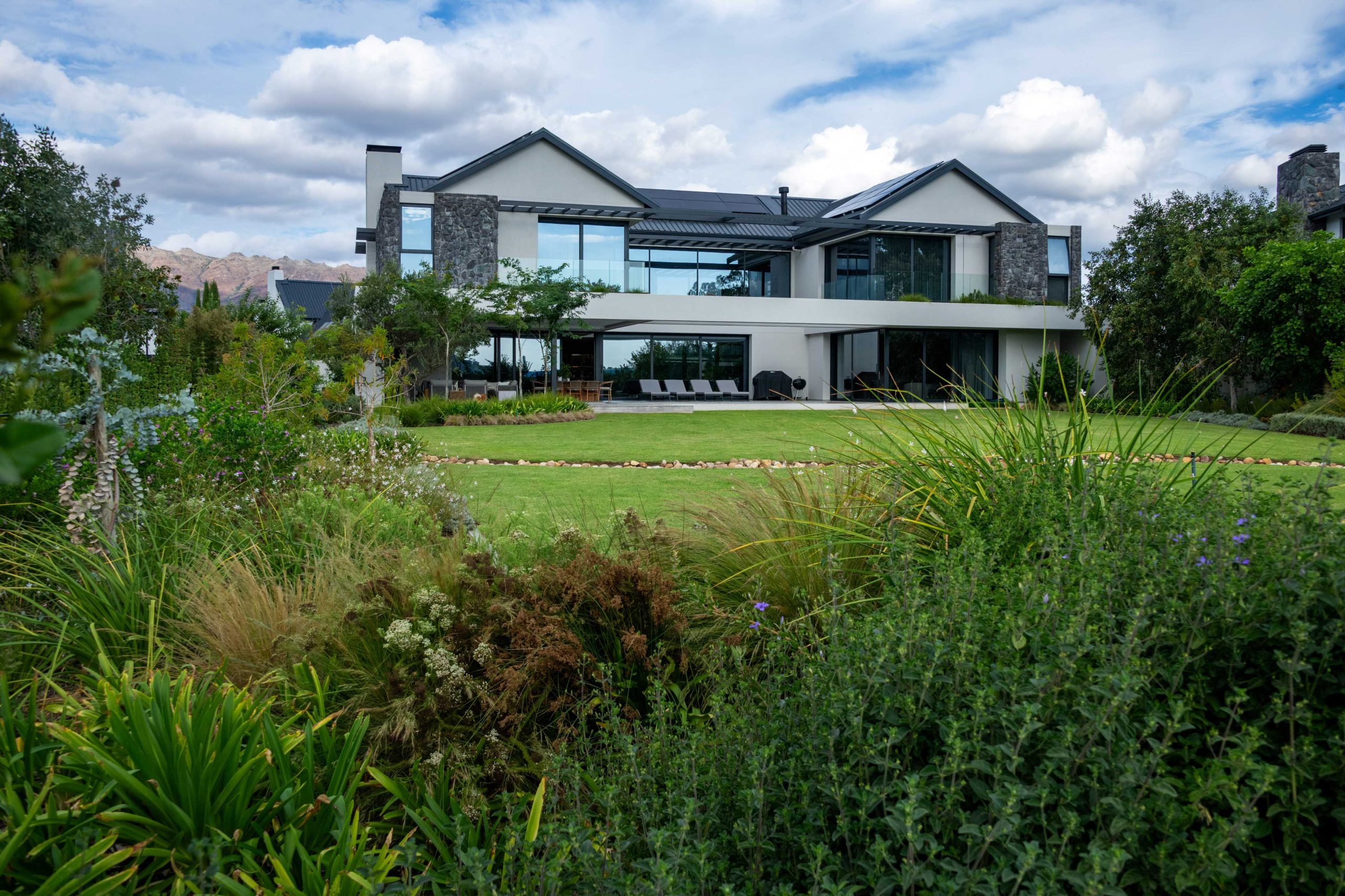 Modern Val de Vie home with open lawn and a river-stone stream by CSA Landscaping, best landscapers in the Boland and Cape Winelands