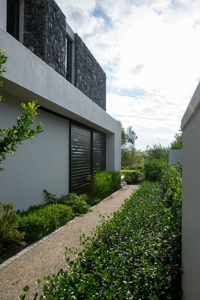 Exposed aggregate side path with low num-num (Carissa) hedging and evergreen shrubs along a contemporary home at Val de Vie Estate, Paarl, by CSA Landscaping — leading landscapers in the Boland and Cape Winelands