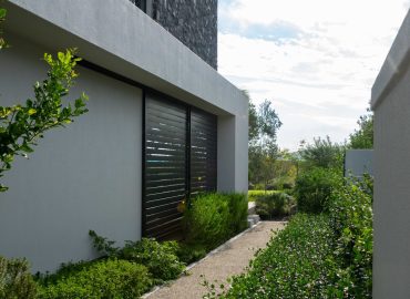 Exposed aggregate side path with low num-num (Carissa) hedging and evergreen shrubs along a contemporary home at Val de Vie Estate, Paarl, by CSA Landscaping — leading landscapers in the Boland and Cape Winelands