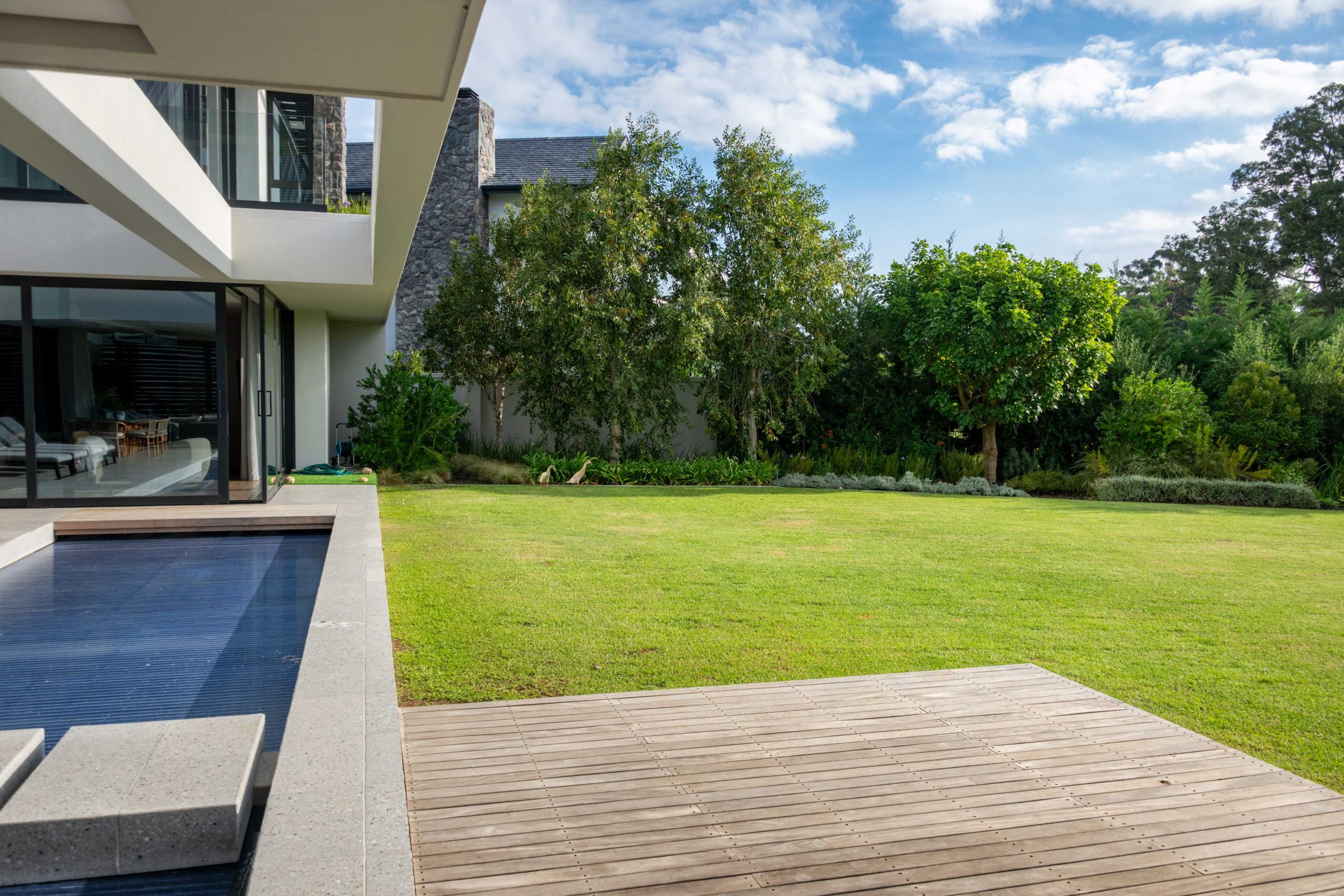 Timber deck and pool terrace opening onto lawn and layered garden beds at a contemporary home in Val de Vie Estate, Paarl, by CSA Landscaping — leading landscapers in the Boland and Cape Winelands