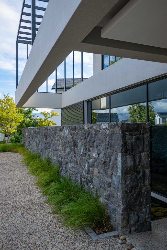 Stone-clad wall with ornamental grasses along the exposed aggregate driveway at Val de Vie Estate, Paarl, by CSA Landscaping — leading landscapers in the Boland and Cape Winelands